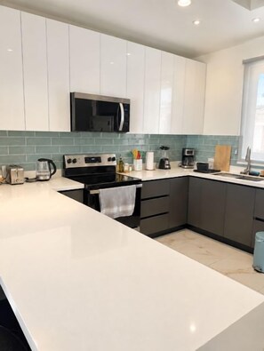 A modern kitchen with white cabinets, a black microwave, and a tiled backsplash. - Blue Wave House I Ocean Villas (Playas Del Coco)