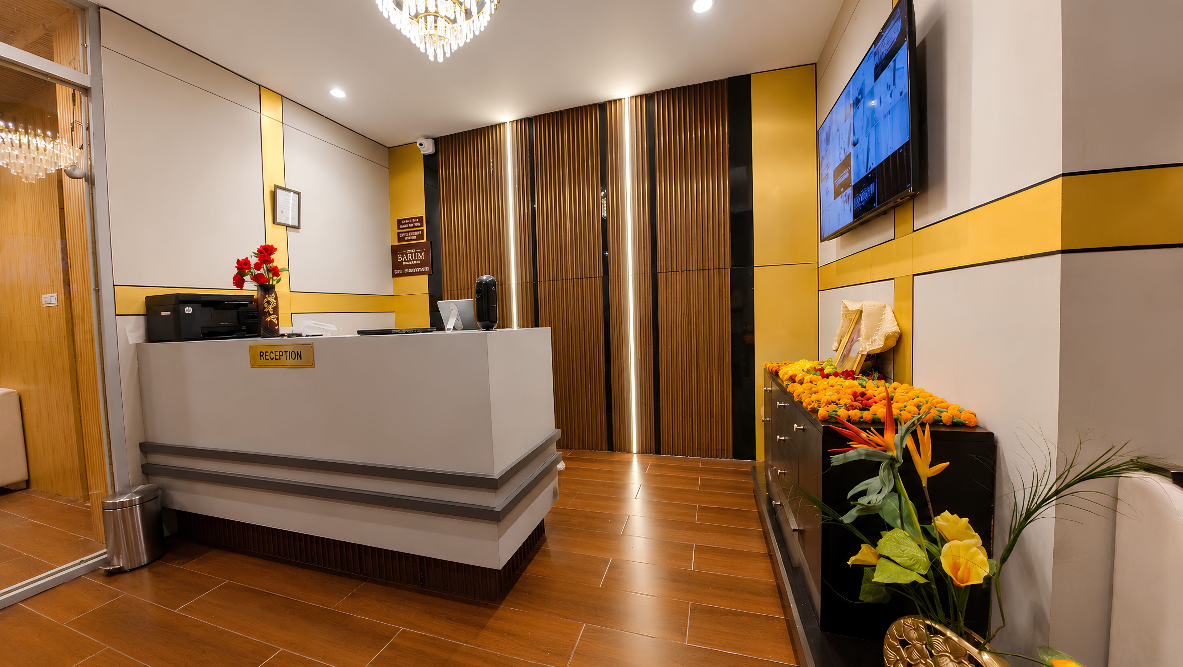 Un área de recepción con mostrador, televisor montado y una planta decorativa.