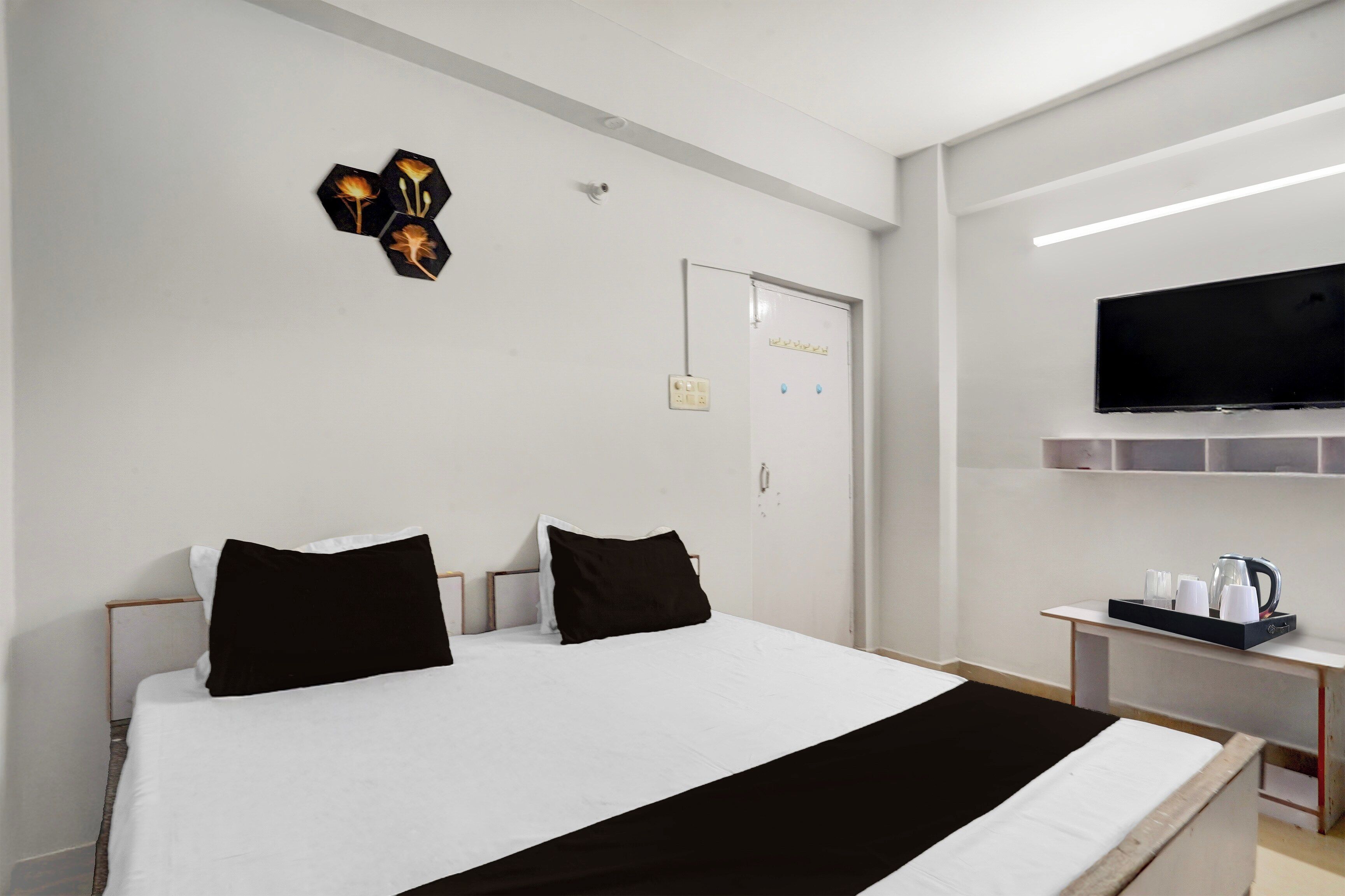 Une chambre d’hôtel avec un lit, un téléviseur fixé au mur et une petite table avec une bouilloire et des tasses.