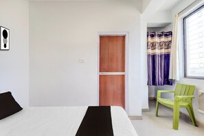 A room with a bed, a wooden door, a window with curtains, and a green chair. - Super Hotel O Digha J.P Setu Patna (Patna)