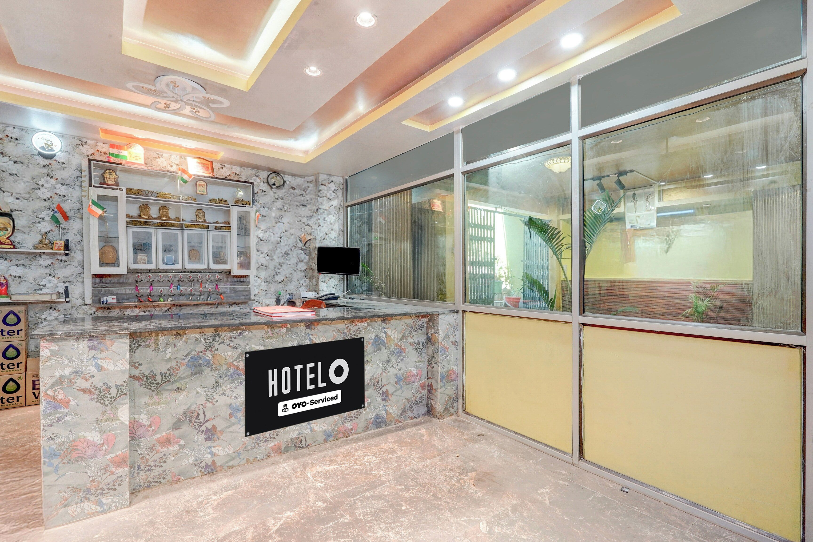 A hotel reception area with a marble counter, a sign indicating it is OYO-Serviced, and a large window offering a view of the outside.