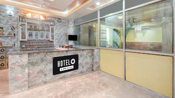 A hotel reception area with a marble counter, a sign indicating it is OYO-Serviced, and a large window offering a view of the outside.