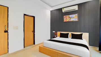 A modern hotel room with a large bed, a wooden headboard, a painting on the wall, and an air conditioning unit.