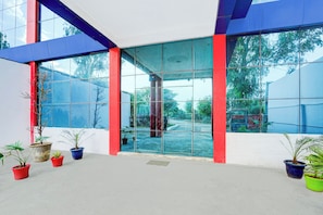 A modern building entrance with large glass doors, potted plants, and a view of the surrounding greenery.
