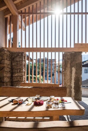 A wooden table with food items and a cup, set against a stone wall and wooden beams, with a view of buildings through a barred window. - Apartment 'Töllhof - Stadl 1' with Mountain View, Balcony and Wi-Fi (Rasa)
