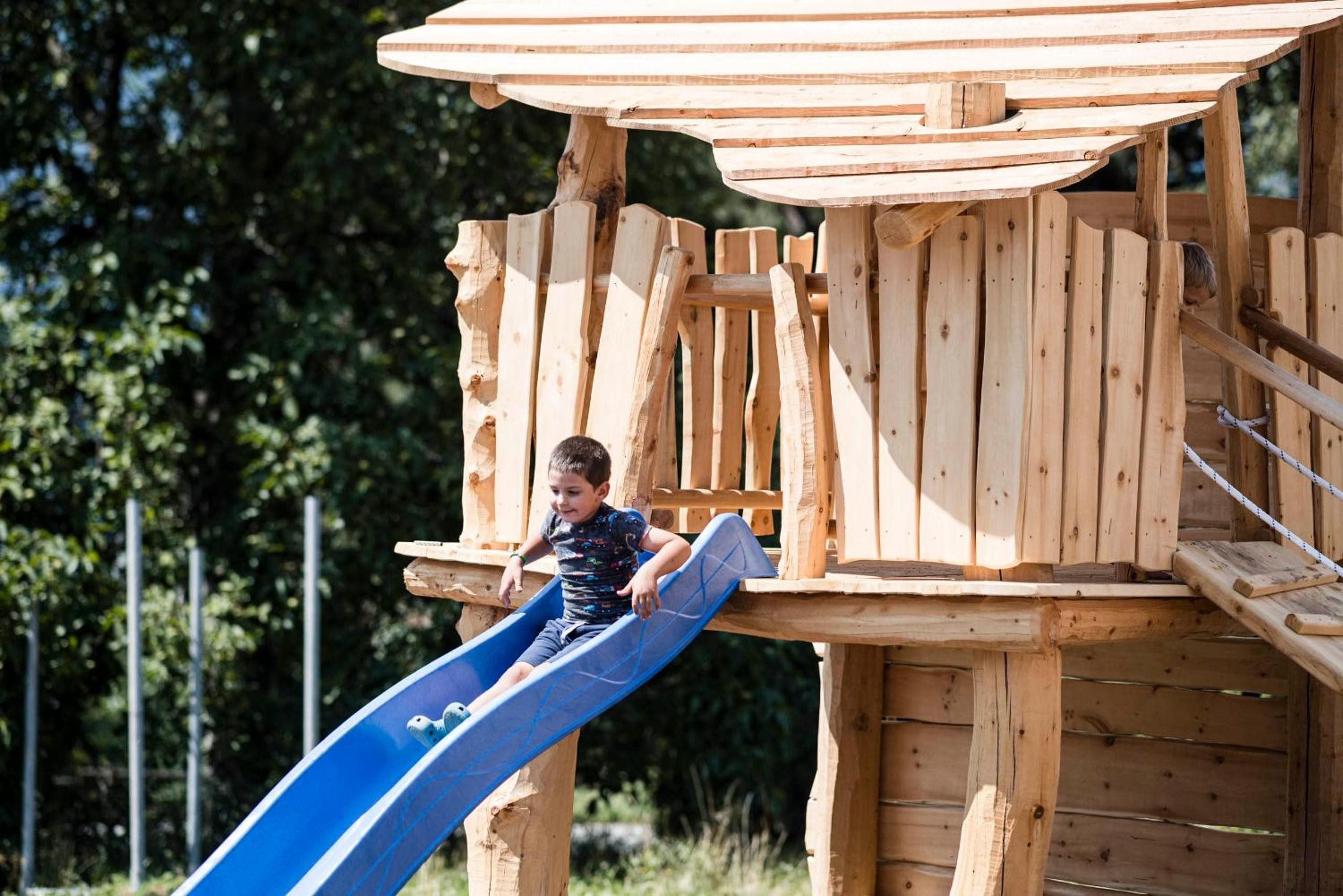 Niño en un tobogán azul unido a una estructura de juegos de madera.