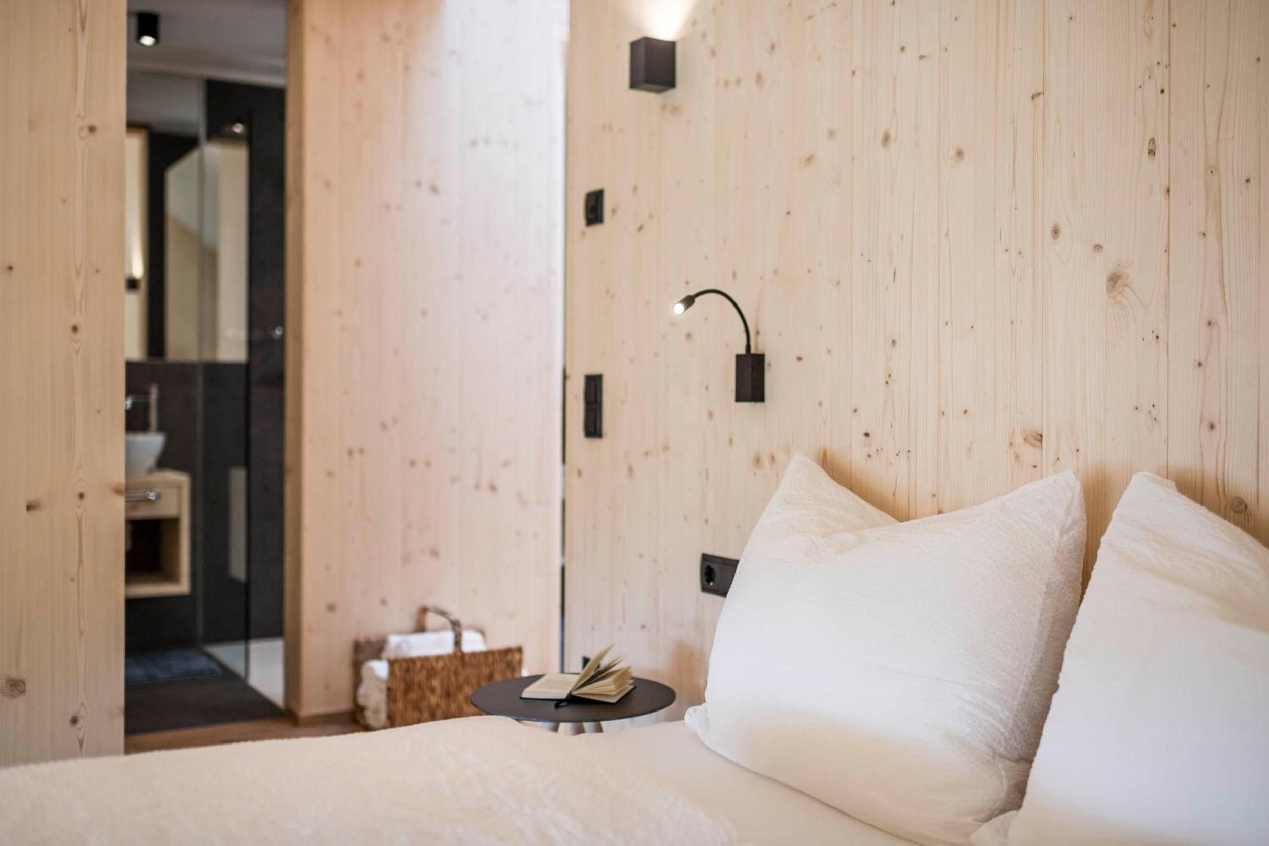 A bedroom with a wooden wall, a bedside table with a book, and a white bed.
