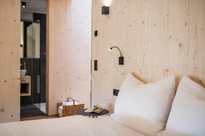 Un dormitorio con pared de madera, una mesita de noche con un libro y una cama blanca.