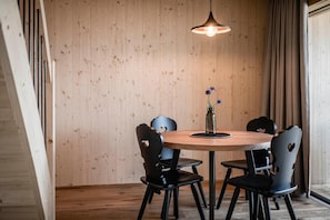 Una mesa de madera redonda con seis sillas, una lámpara colgante y un florero con flores sobre la mesa.