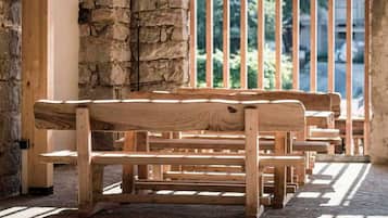 A wooden bench area with a stone wall and a view of greenery through a railing.