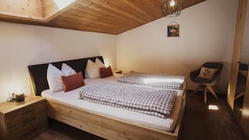 A bedroom with a wooden bed, two pillows, a bedside table, a chair, and a hanging light fixture.