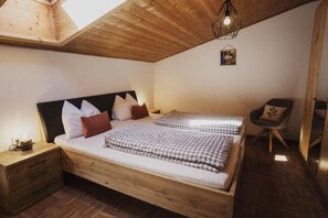 A bedroom with a wooden bed, two pillows, a bedside table, a chair, and a hanging light fixture. - Apartment 'Töllhof Apartments and Farm - Leo' with Mountain View and Wi-Fi (Rasa)