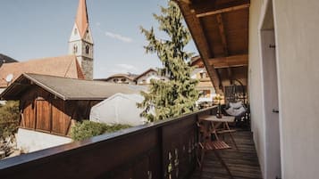 A wooden balcony with a view of a church steeple and a white tent-like structure.