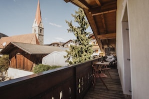 A wooden balcony with a view of a church steeple and a white tent-like structure. - Apartment 'Töllhof Apartments and Farm - Leo' with Mountain View and Wi-Fi (Rasa)