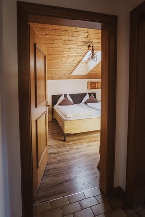 A bedroom with a wooden floor, a bed with a headboard, and a sloped ceiling with a hanging light fixture. - Apartment 'Töllhof - Paul' with Mountain View and Wi-Fi (Rasa)