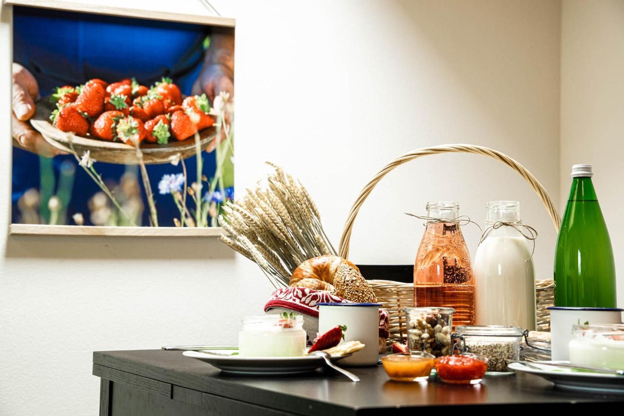 Un desayuno con una cesta de fresas, una hogaza de pan y diferentes productos para el desayuno sobre una mesa.