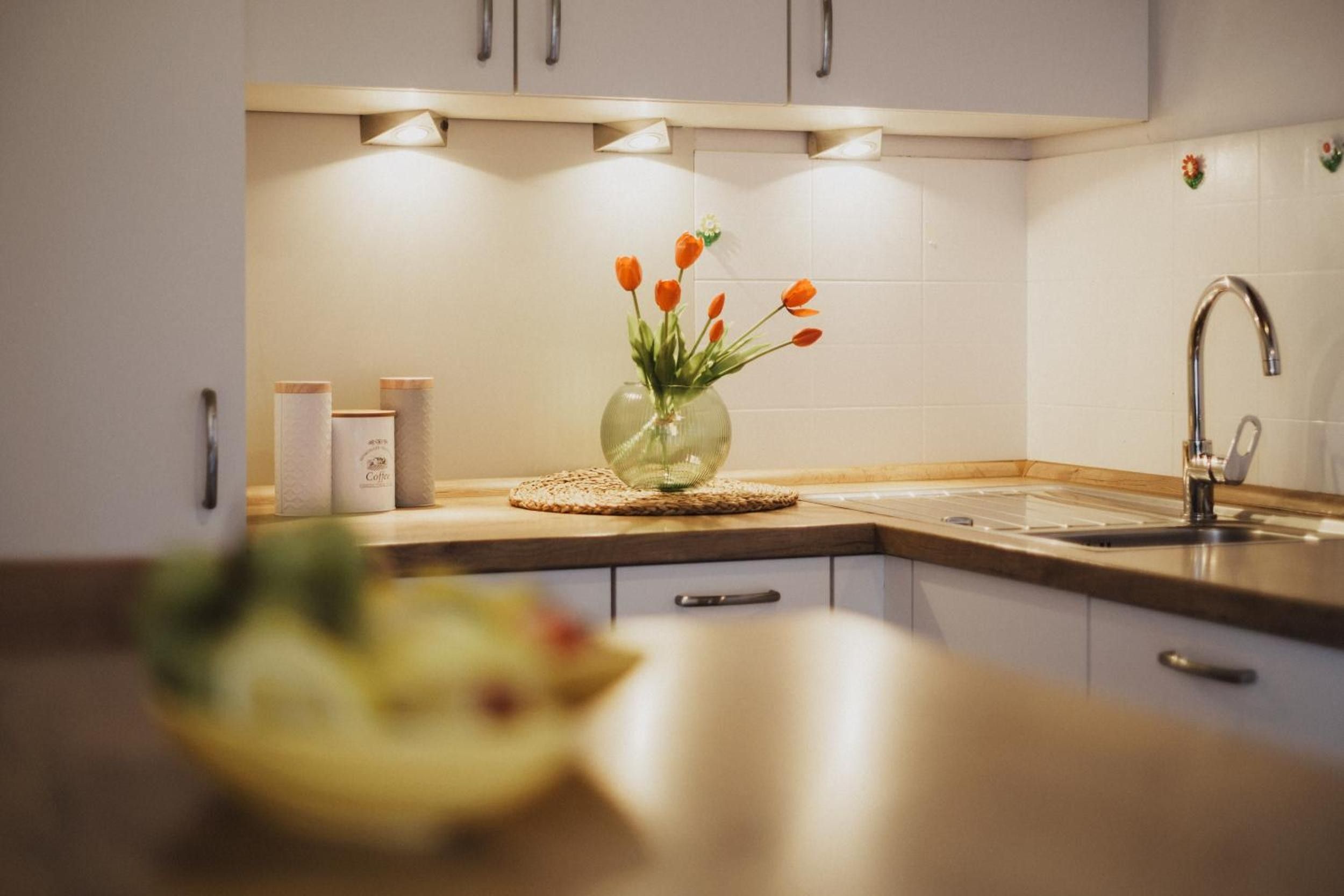 A kitchen with white cabinets, a stainless steel sink, and a vase with orange flowers on the counter.