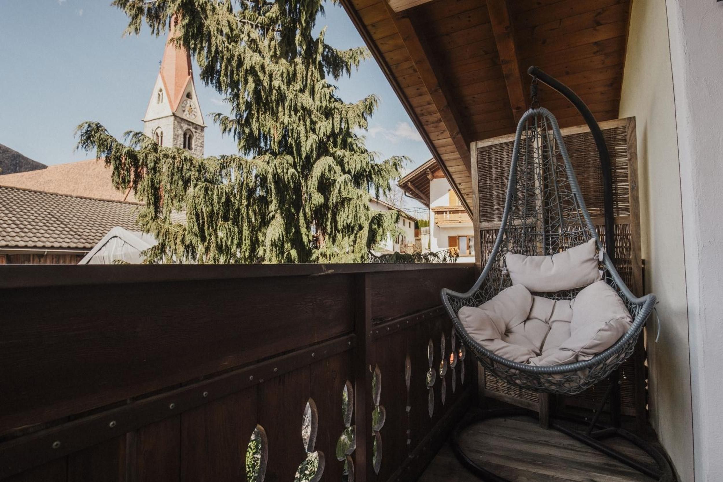 Un balcon en bois avec un fauteuil suspendu et une vue sur le clocher d’une église.