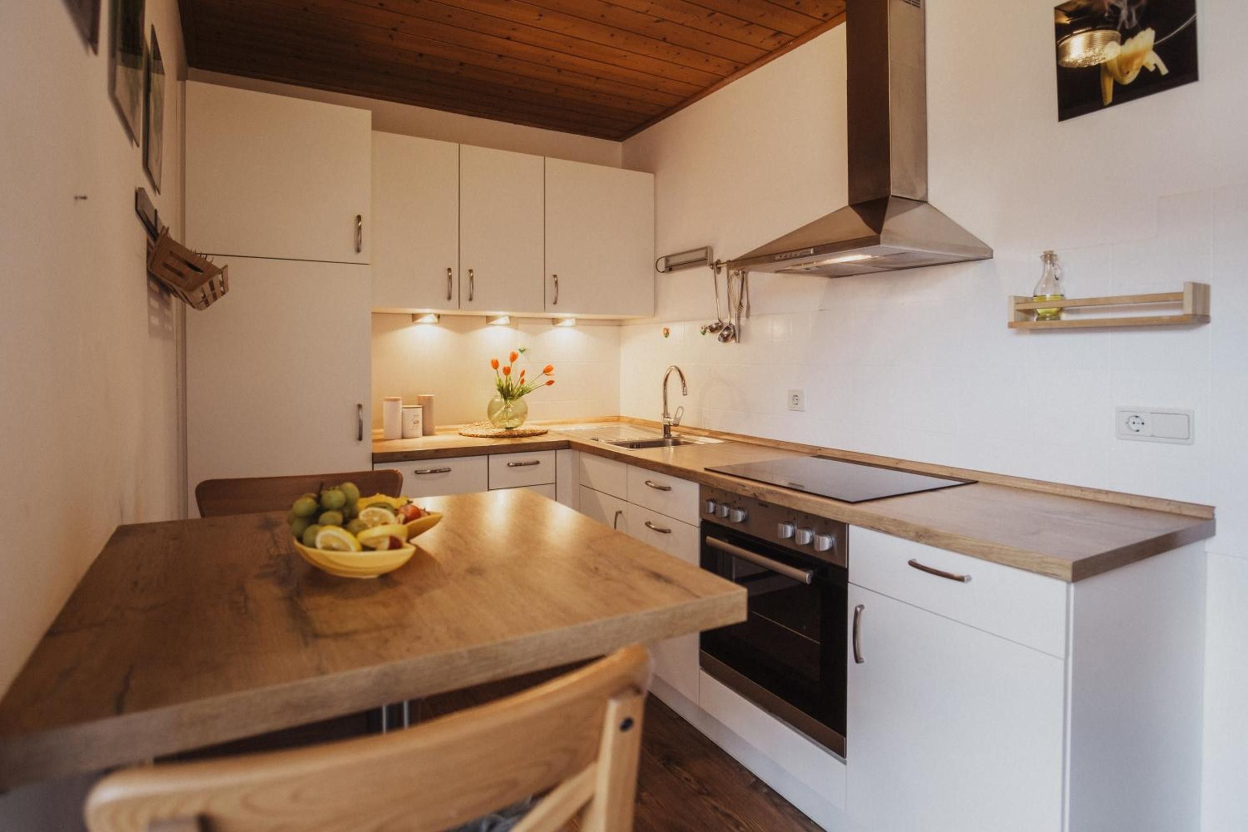 Una cocina moderna con armarios blancos, encimera de madera, horno empotrado y campana extractora de acero inoxidable.