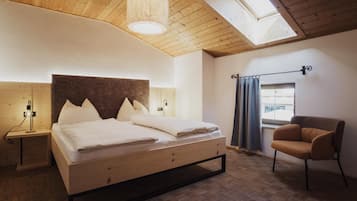 A bedroom with a bed, a chair, a nightstand, a lamp, a window with curtains, and a skylight.