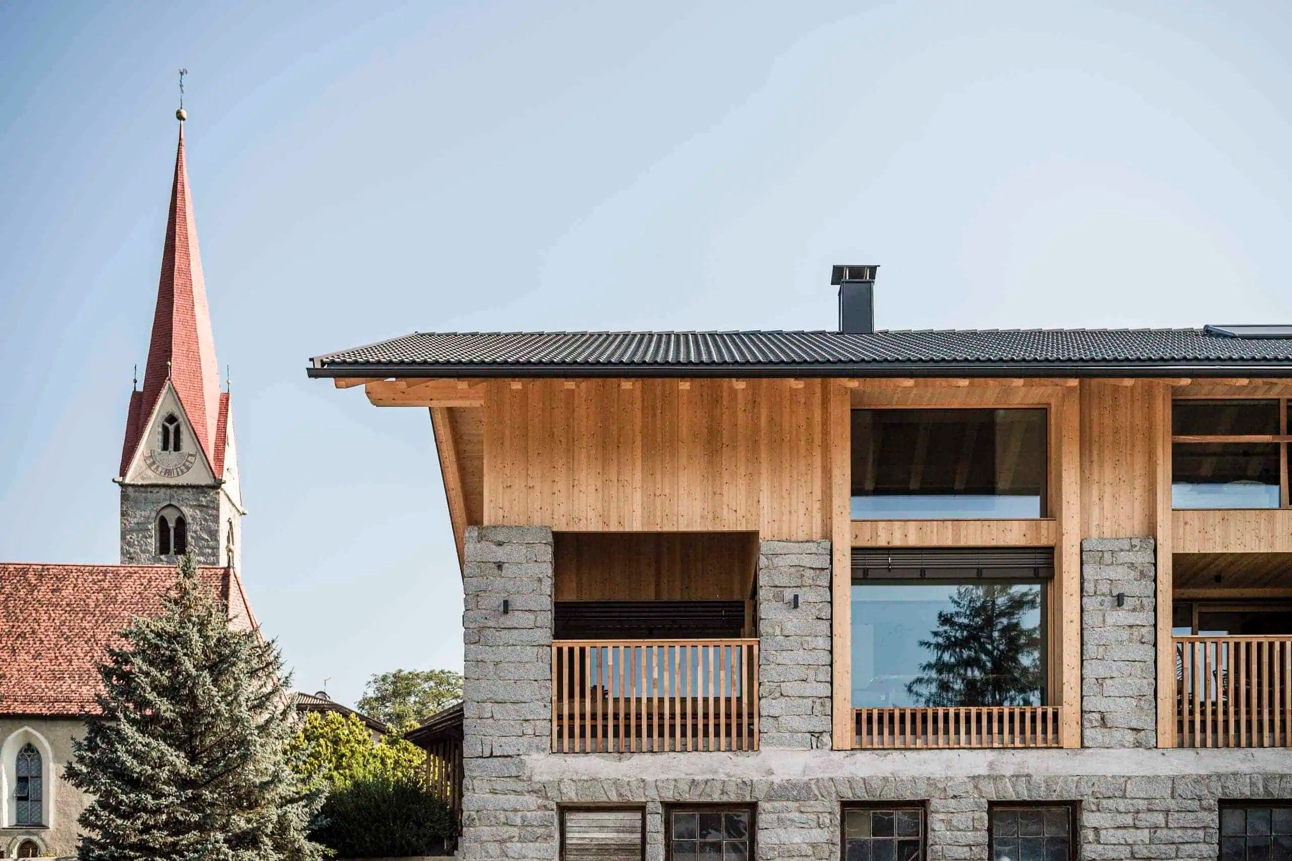 Un edificio moderno de dos pisos con fachada de madera, ventanas amplias y base de piedra.