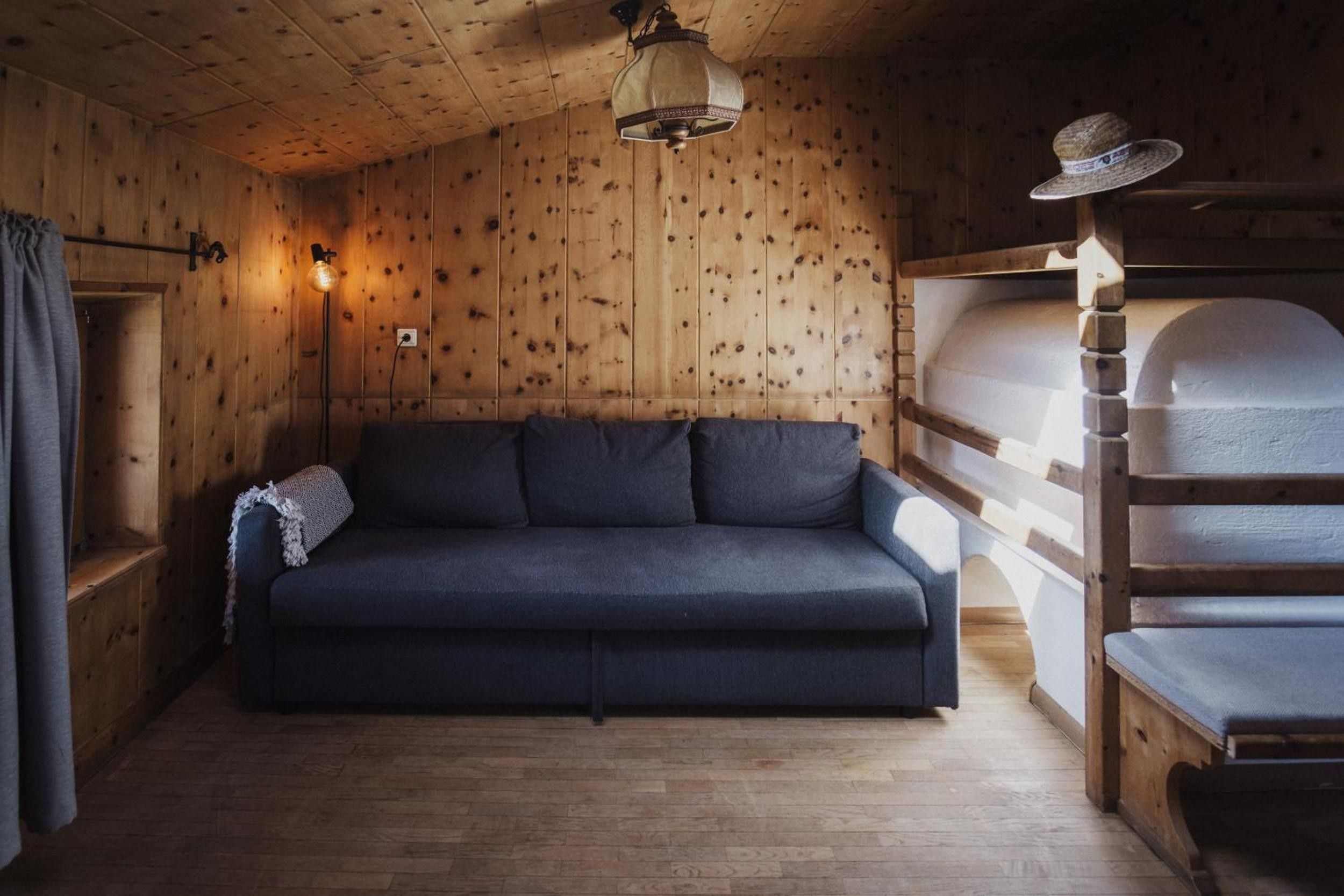 A wooden cabin interior with a sofa, a hanging light fixture, and a bunk bed.