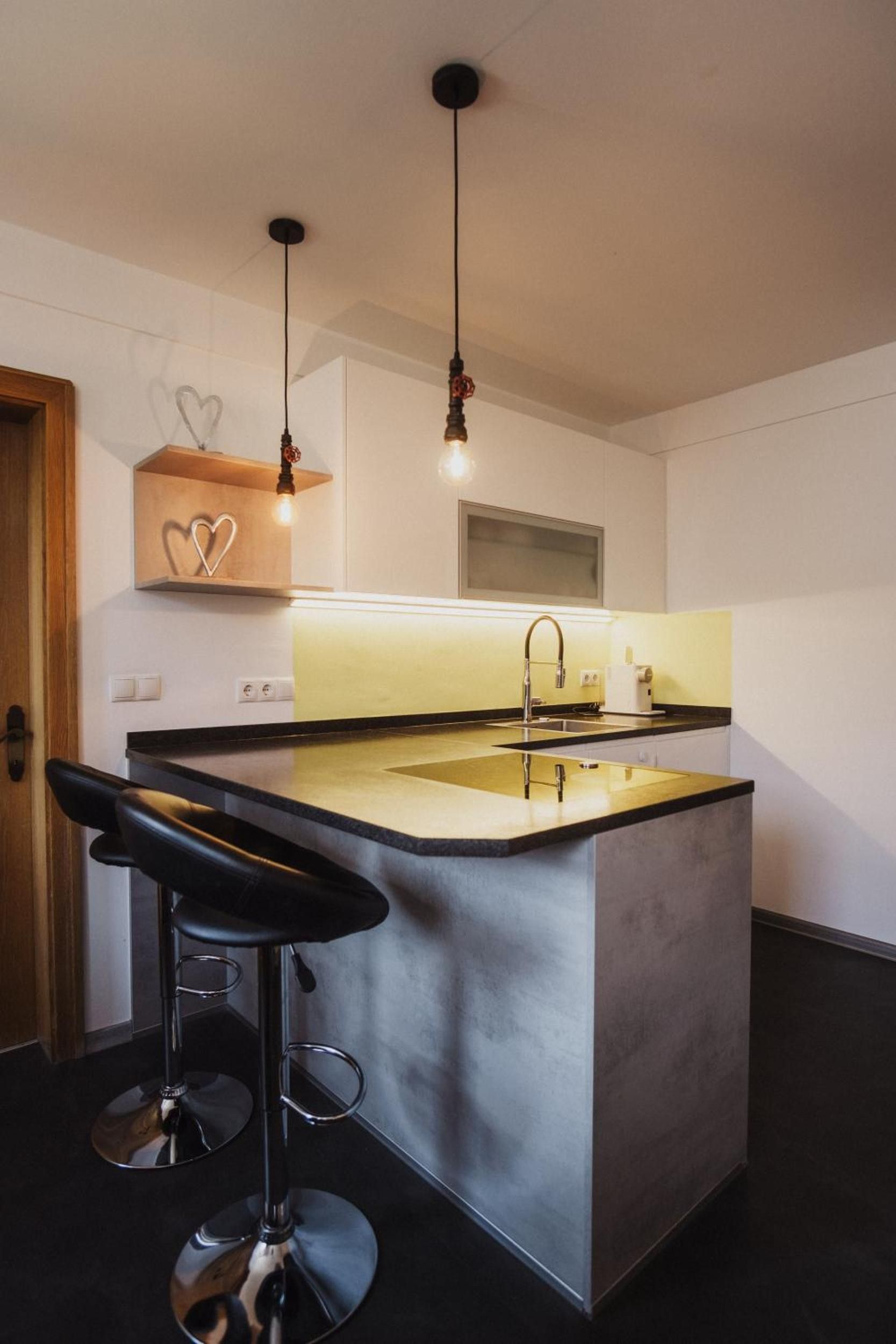 Eine moderne Küche mit einer zentralen Kochinsel, Barhocker, Pendelleuchten und einem herzförmigen Regal aus Holz.