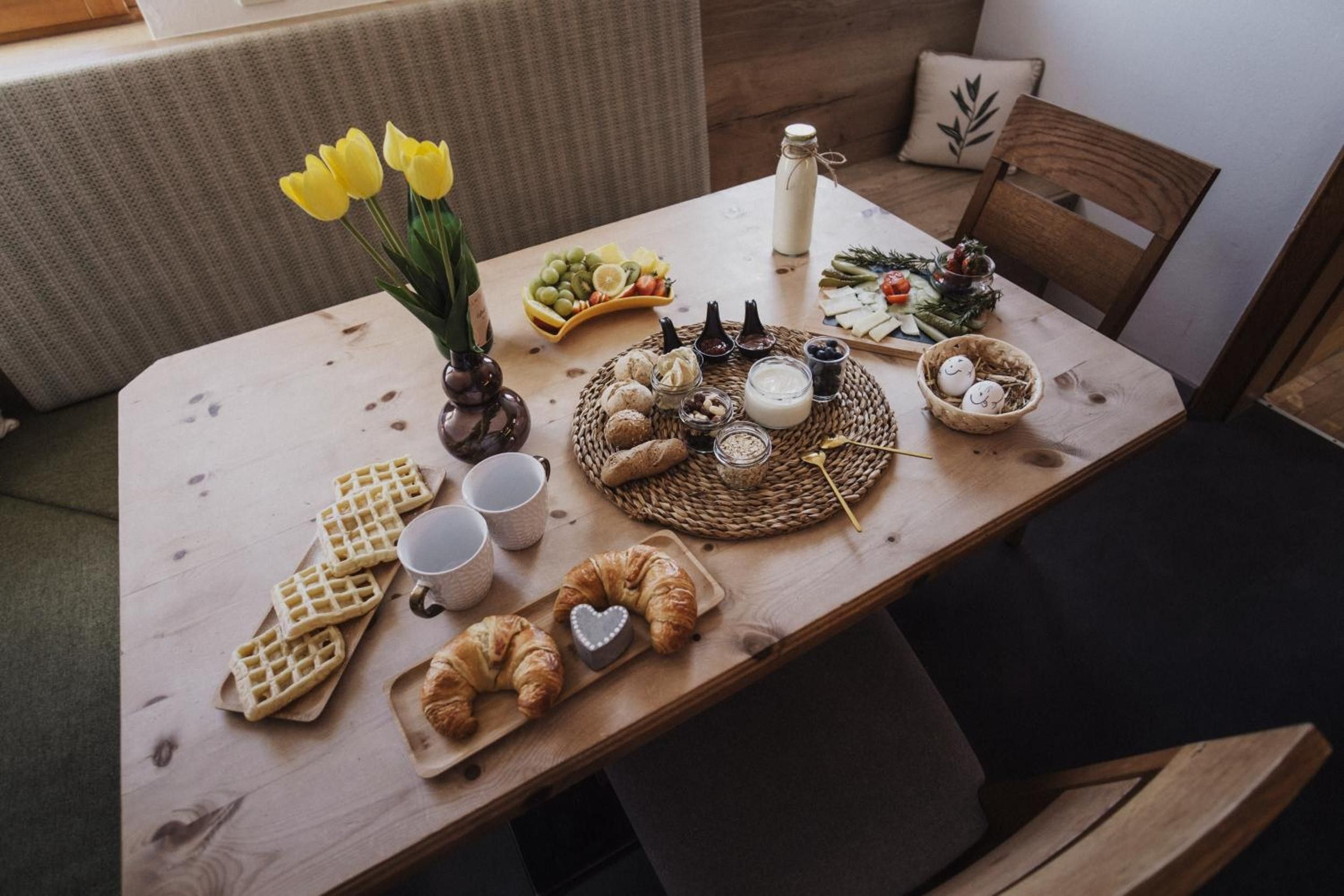 Una mesa de madera con diversos alimentos, como waffles, croissants y una botella de leche.