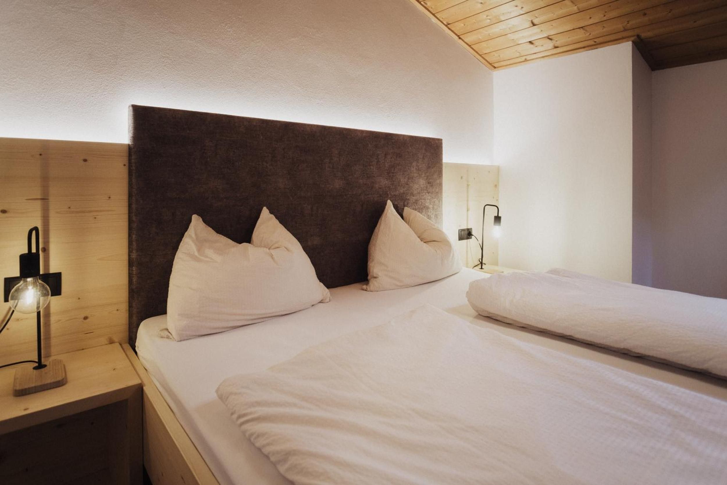 Ein Schlafzimmer mit einem hölzernen Kopfteil, zwei weißen Kissen, einer Nachttischlampe und einem Bett mit weißer Bettwäsche.