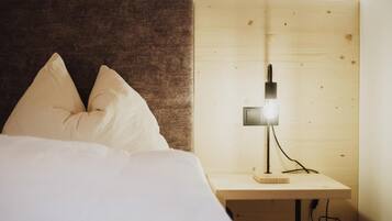 Una cama con ropa de cama blanca y dos almohadas, una mesita de noche con una lámpara y un cabecero de madera.