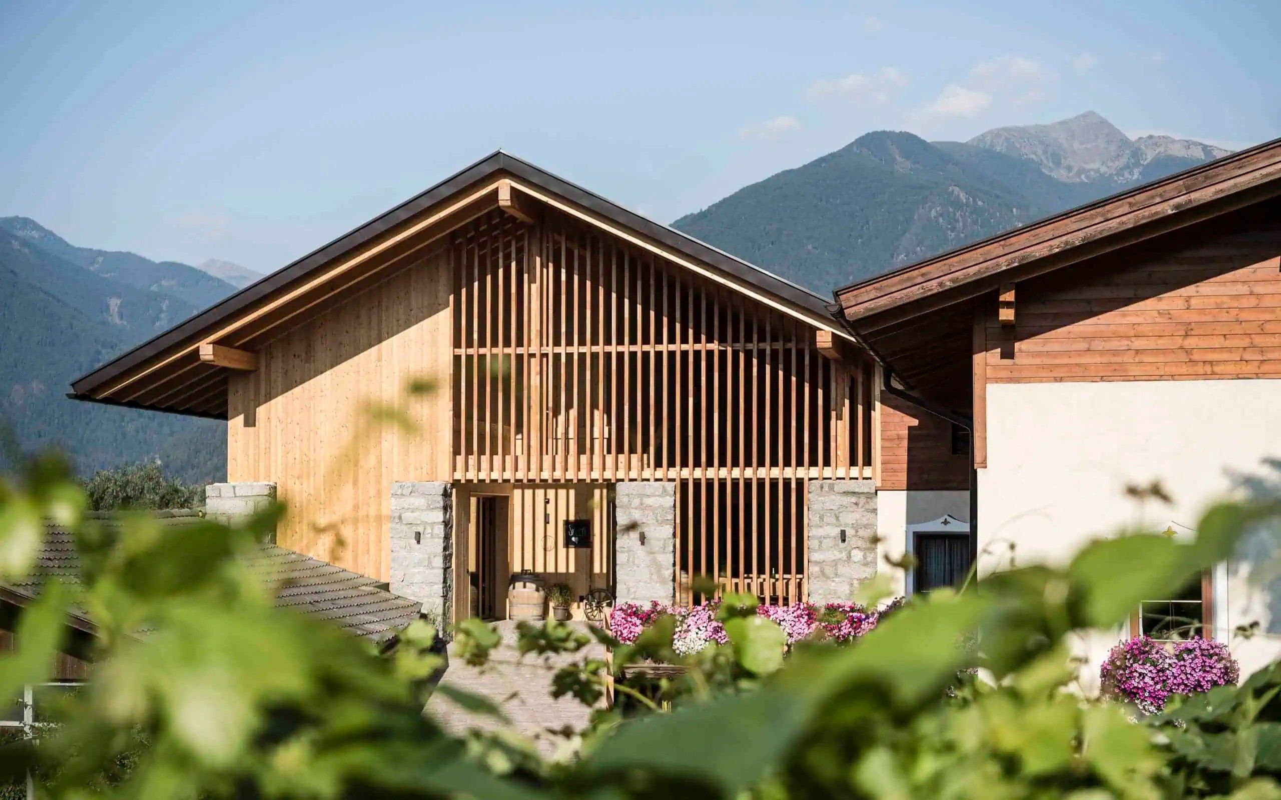 A wooden cabin with a stone foundation, set against a mountainous backdrop.