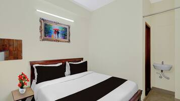 A bedroom with a bed, a nightstand with a vase of flowers, a painting on the wall, and a bathroom with a sink.