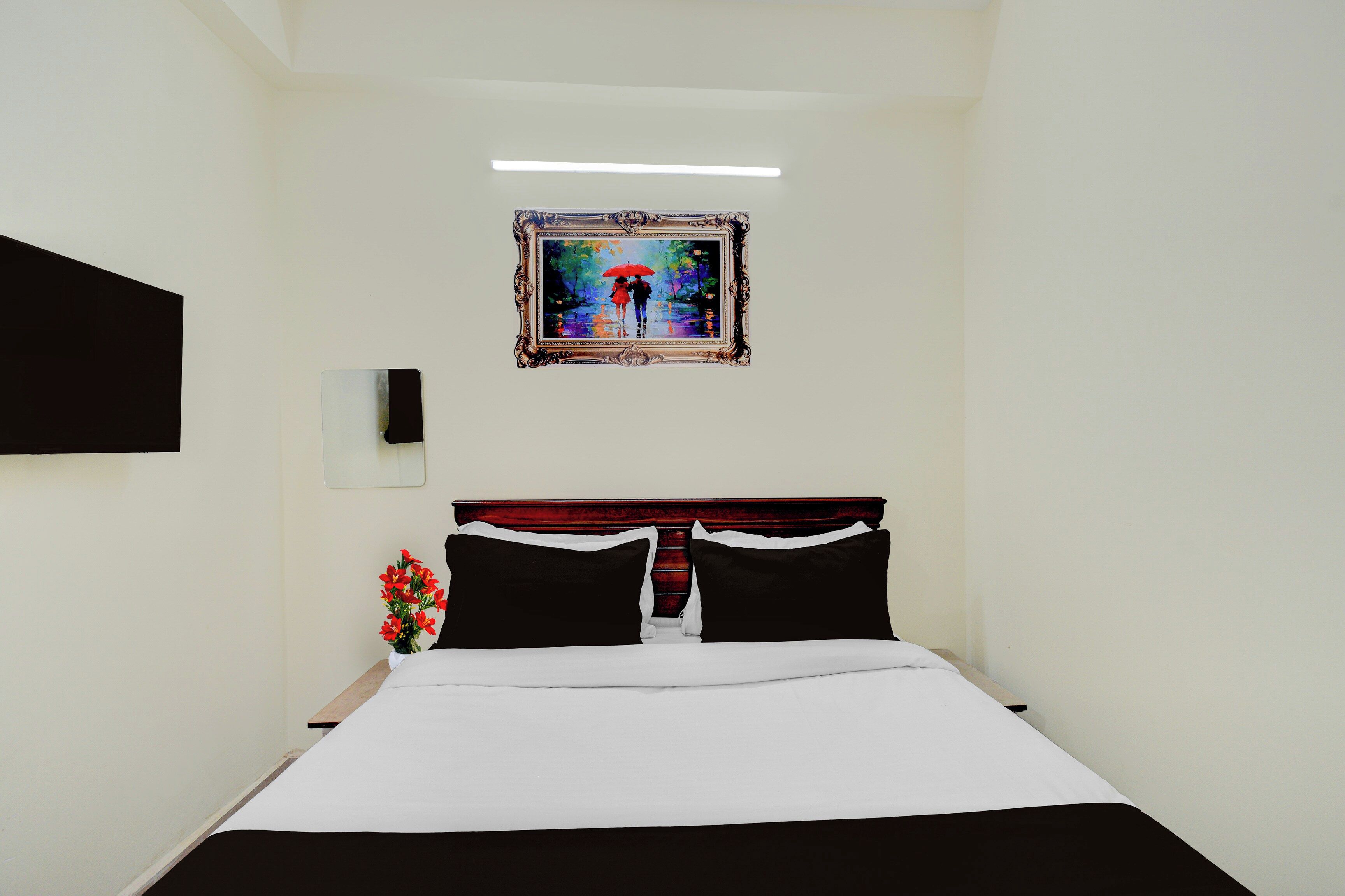 Una habitación de hotel con una cama, una mesita de noche, un florero con flores y un cuadro en la pared.