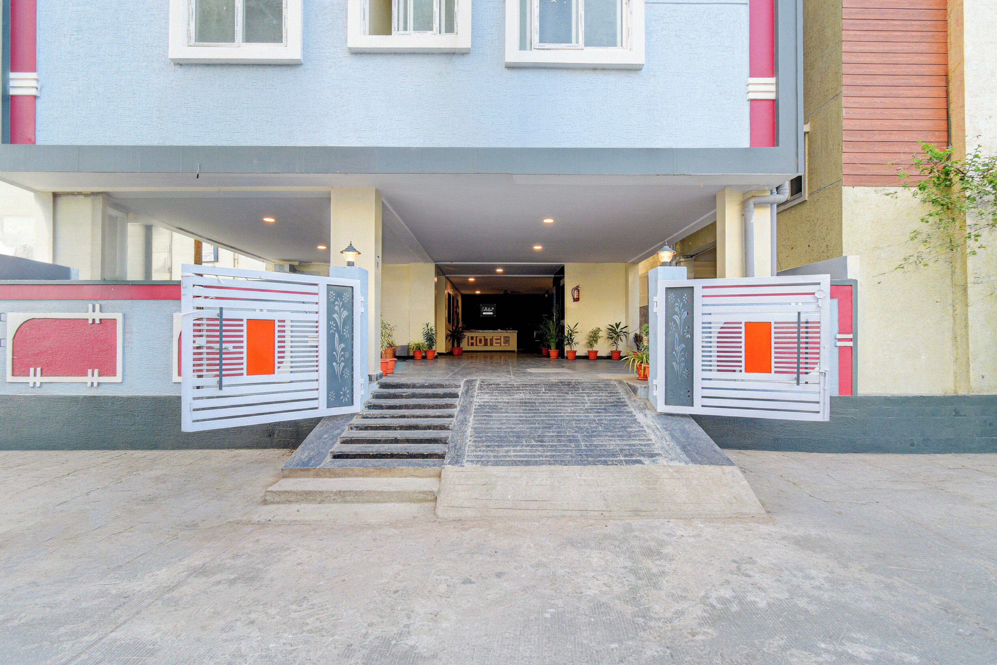 Entrada de un hotel con una escalera que conduce a la recepción, un extintor y plantas en macetas.