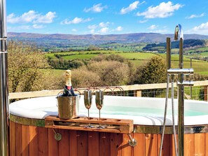 Een hottub met champagne en twee glazen op een houten terras, met uitzicht op een schilderachtig landschap.