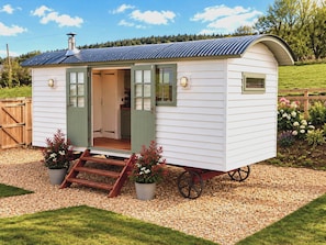 A small, single-story mobile home with a porch, a set of steps leading to the entrance, and a wheelbarrow in front. - Oak Hut (Bishops Castle)
