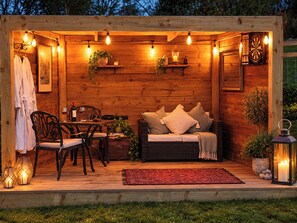 A wooden outdoor seating area with a table, chairs, a sofa, and a red rug. - Oak Hut (Bishops Castle)