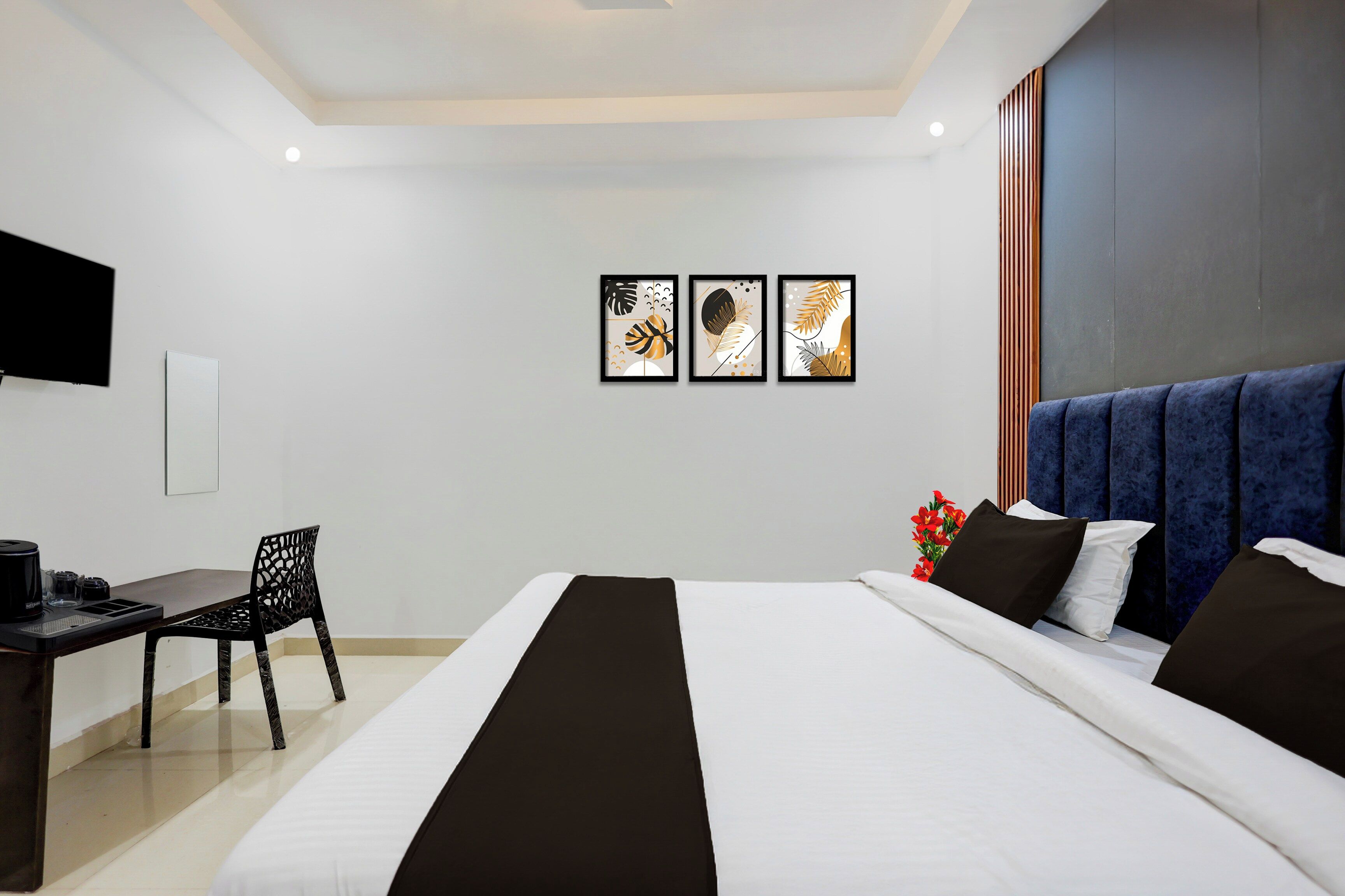 A hotel room with a bed, a desk, a chair, and three framed artworks on the wall.