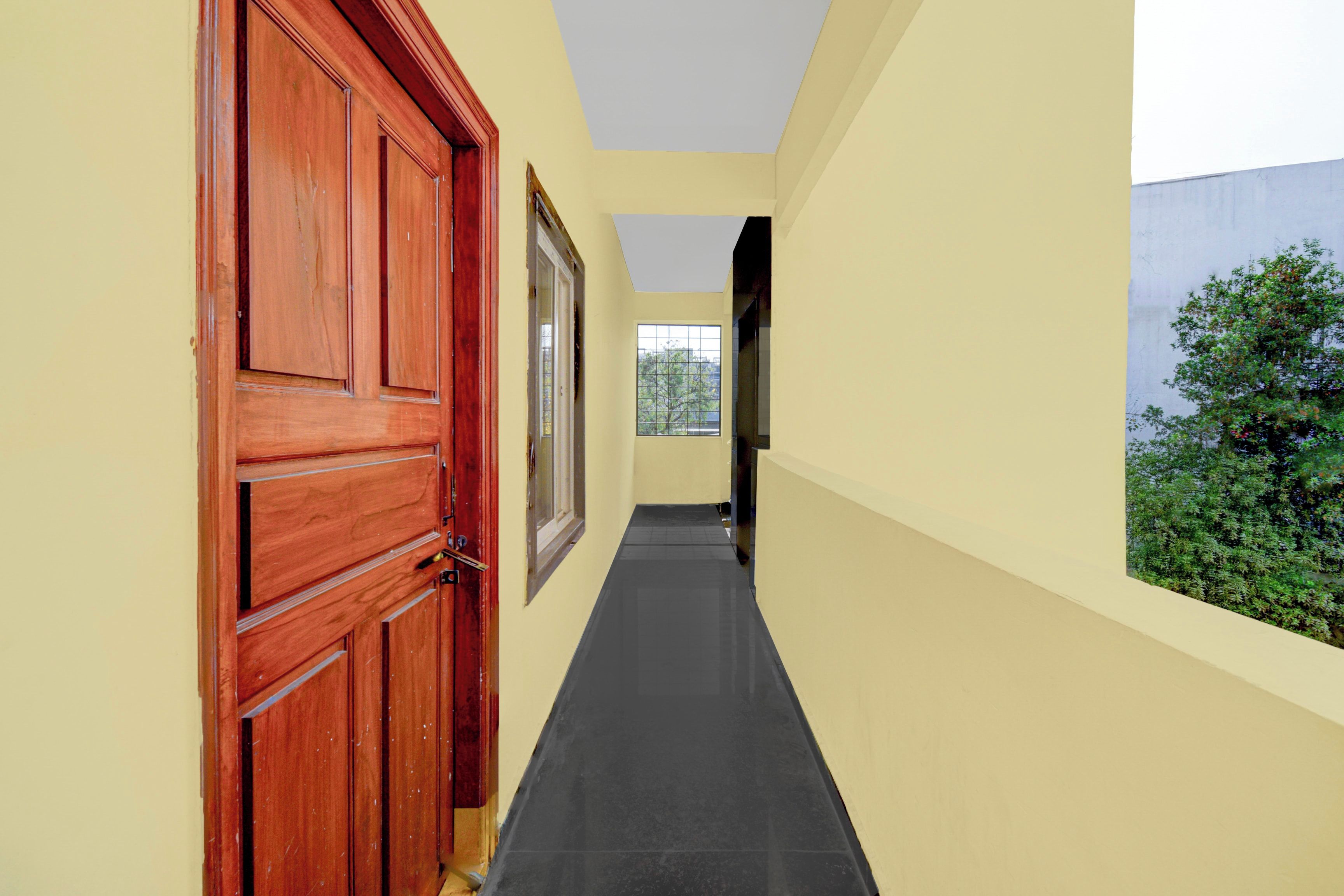 A narrow hallway with a wooden door and a window, leading to a room with a view of greenery.
