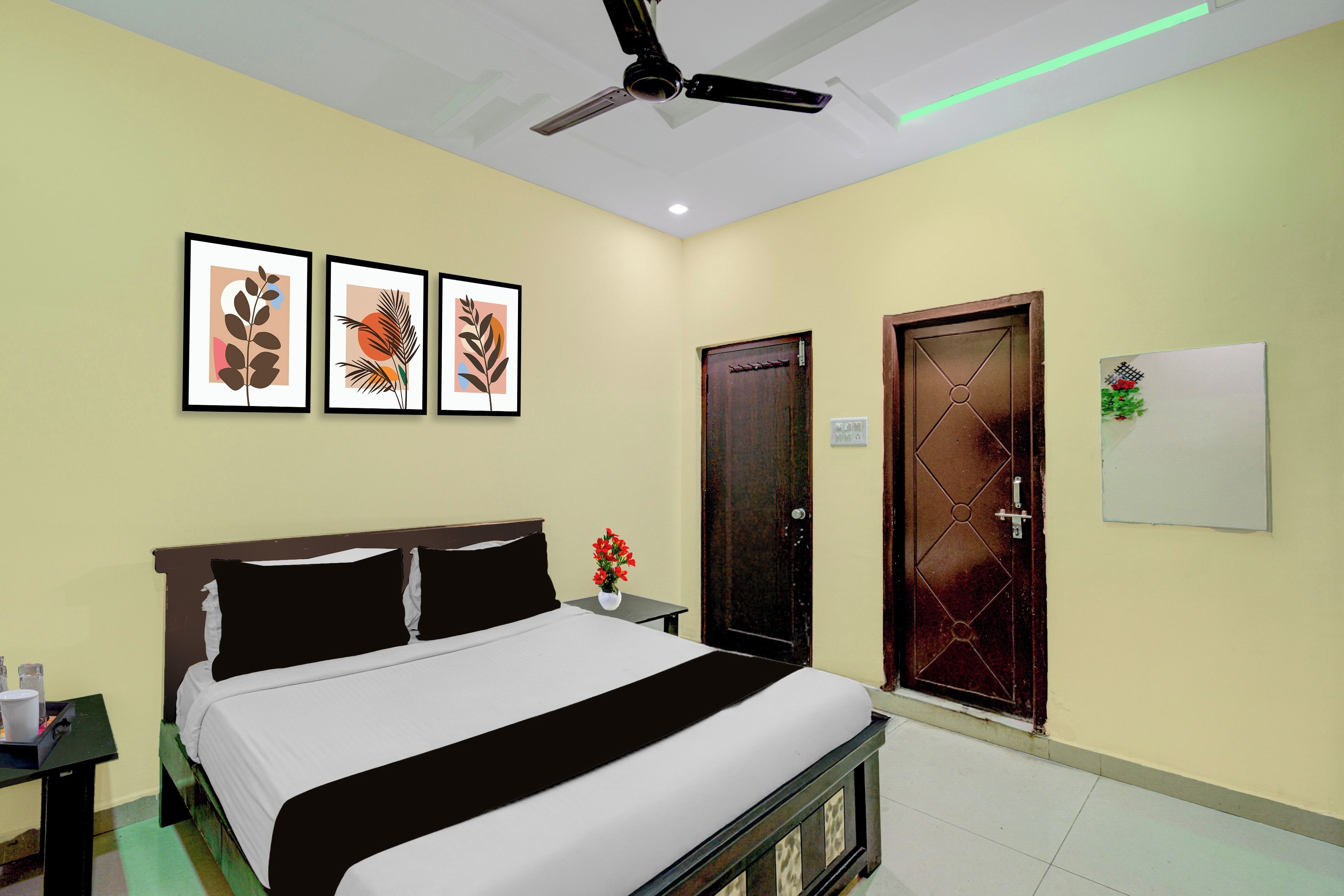 A hotel room with a bed, a ceiling fan, and three framed artworks on the wall.