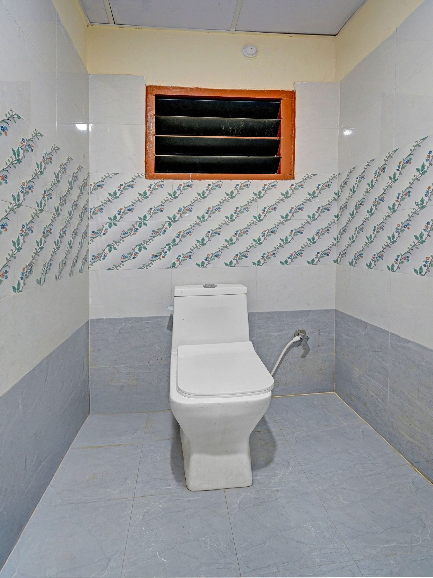 Une petite salle de bain avec des toilettes, une fenêtre et des murs carrelés.