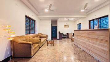 A spacious living area with a sofa set, a wooden reception desk, and a ceiling fan.