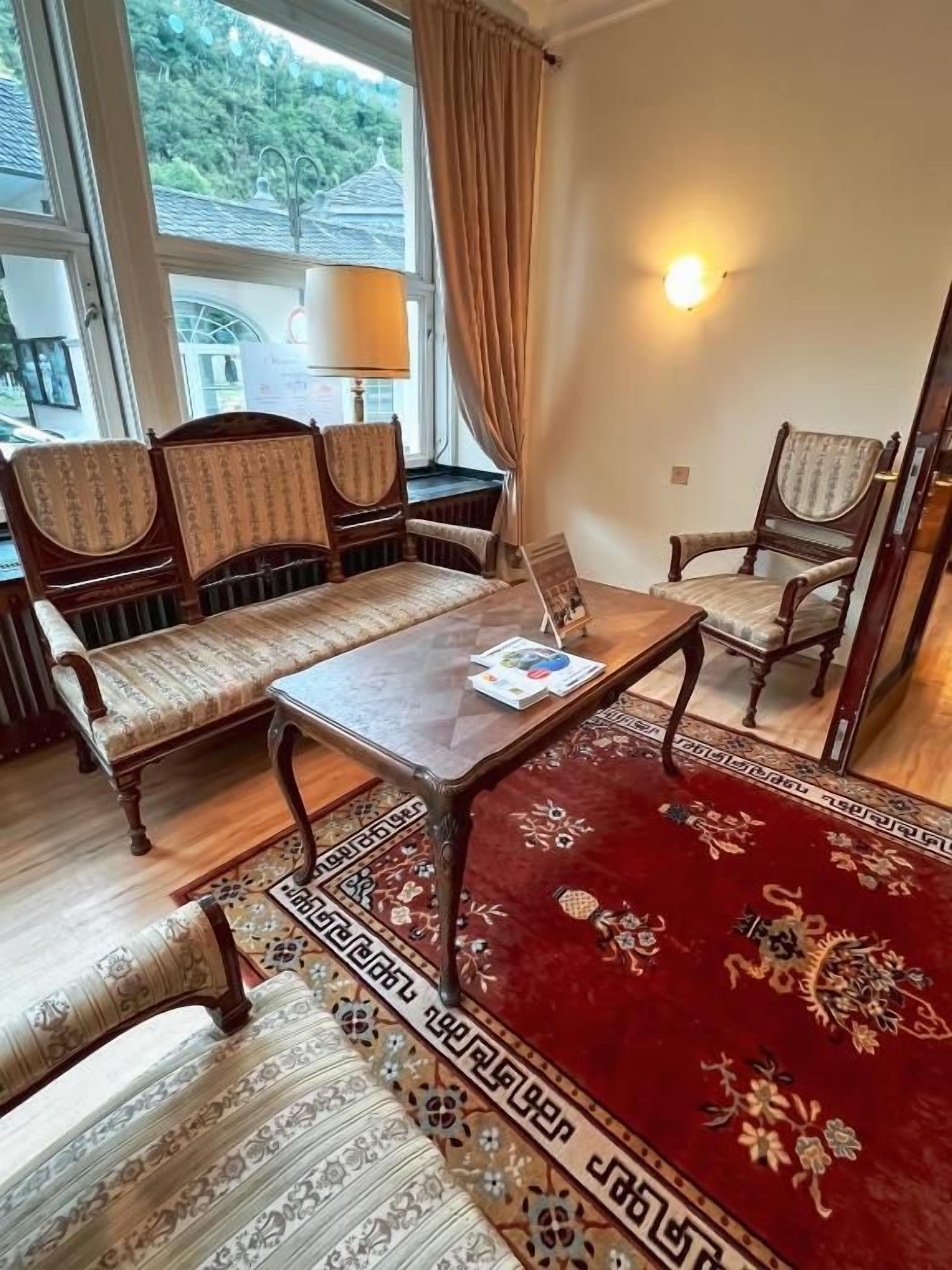 Ein Zimmer mit einer Couch, einem Tisch, einem Stuhl, einem Teppich und einem Fenster mit Vorhängen.