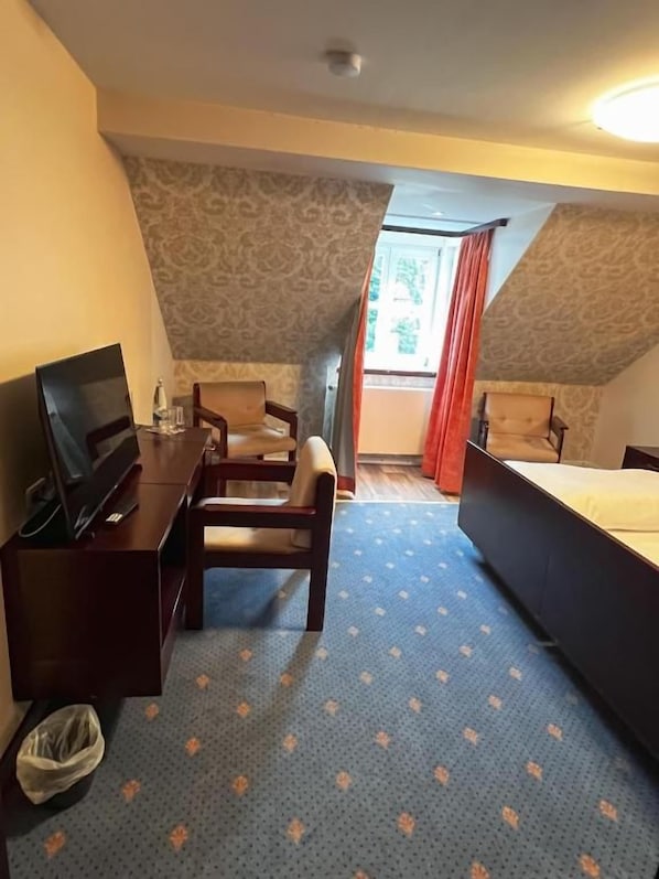 A hotel room with a bed, a desk, a chair, and a television.