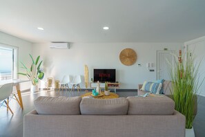 A modern living room with a grey sofa, a TV on the wall, and various decorative items including plants and a round wall hanging. - Silver Villa with private pool and sea view (Atalaia)