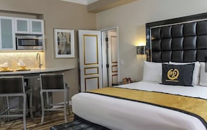 Habitación de hotel con cama, escritorio con sillas, microondas y puerta con marco dorado.