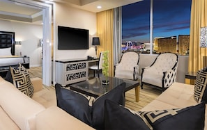 Una habitación de hotel moderna con un ventanal grande, un televisor de pantalla plana, un sofá, dos sillones y una mesa de centro.