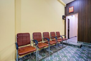 A row of brown chairs with metal frames, a tiled floor with a geometric pattern, and a wooden wall with a framed picture. - Super Hotel O Sant Ravidas Ghat Varanasi (Varanasi)