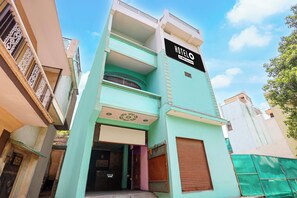A multi-story building with a sign indicating it is a hotel. There are balconies on the upper floors, and the entrance is visible with a closed shutter. - Super Hotel O Sant Ravidas Ghat Varanasi (Varanasi)