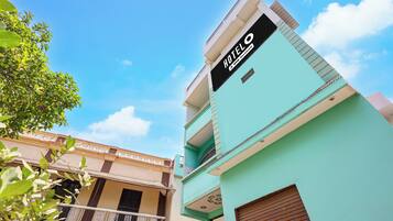 A hotel with a sign indicating it is oyo-serviced, a balcony with decorative railings, and a clear blue sky in the background.